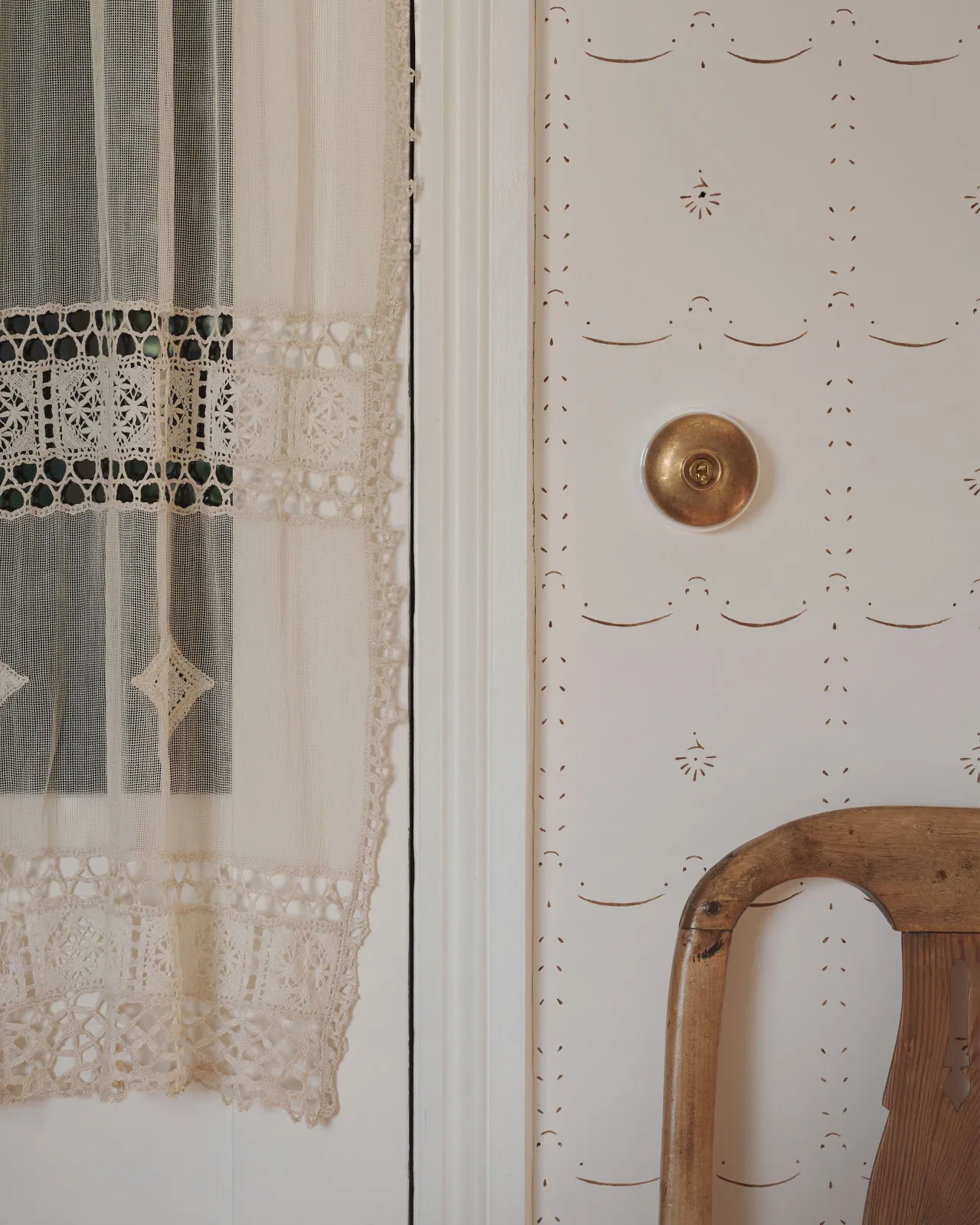 An Aged Brass deVOL Dolly Toggle Switch with white ceramic base, fitted to a wall of deVOL Ditsy Delft Wallpaper in Sepia.
