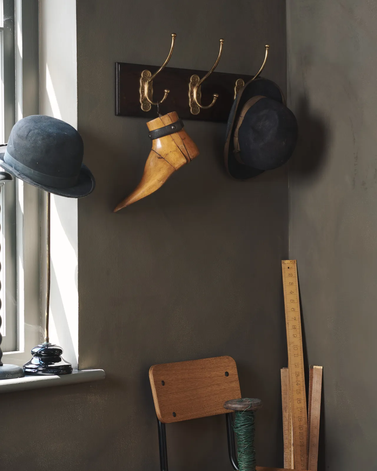 An oblique view of a Mahogany Finish Hook Rack with three brass Grand Parisian Café Hooks, fitted to a dark corner with bowler hats and a vintage wooden shoe tree.