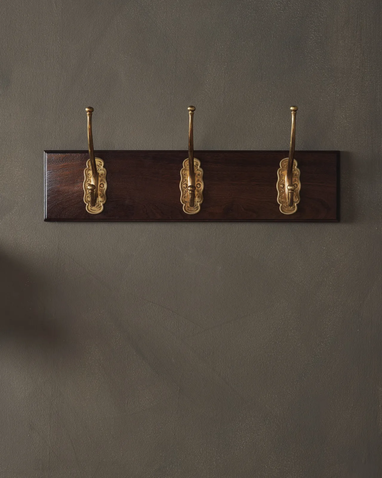 A close-up view of a Mahogany Finish Hook Rack with three brass Grand Parisian Café Hooks.