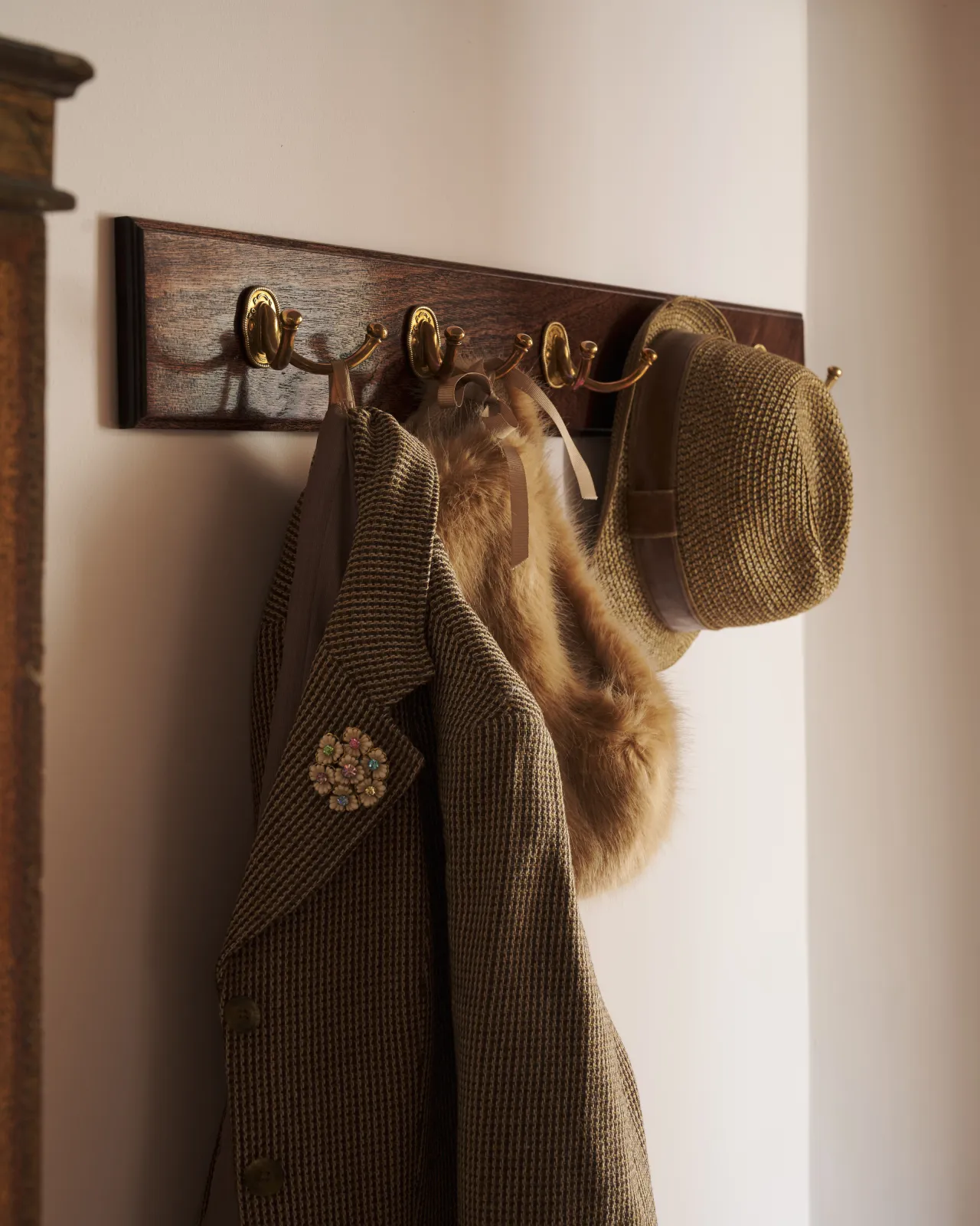 A close-up view of five Twin Parisian Café Hooks on a Mahogany Finish backboard with a tweed jacket and hat hanging.