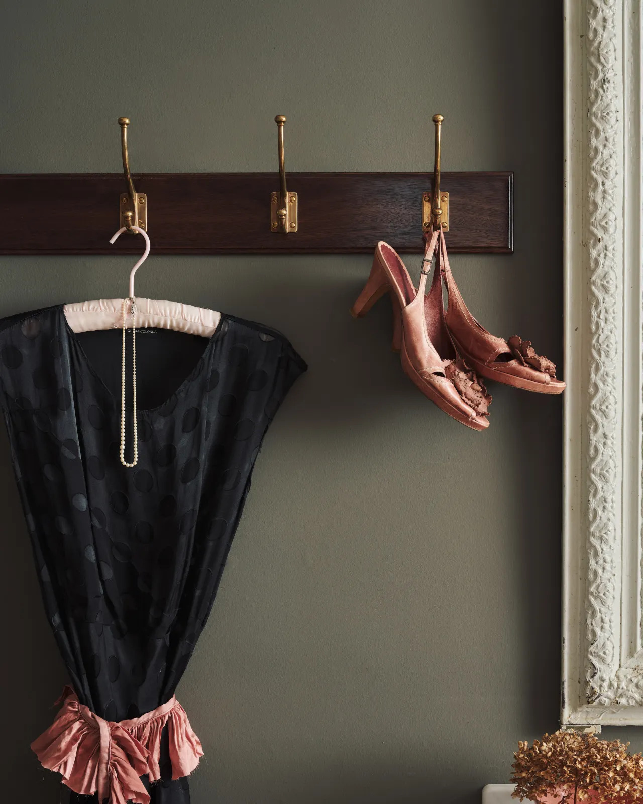 A black lace dress and dusky pink shoes hang from a Mahogany Finish Hook Rack with Edwardian brass hooks.