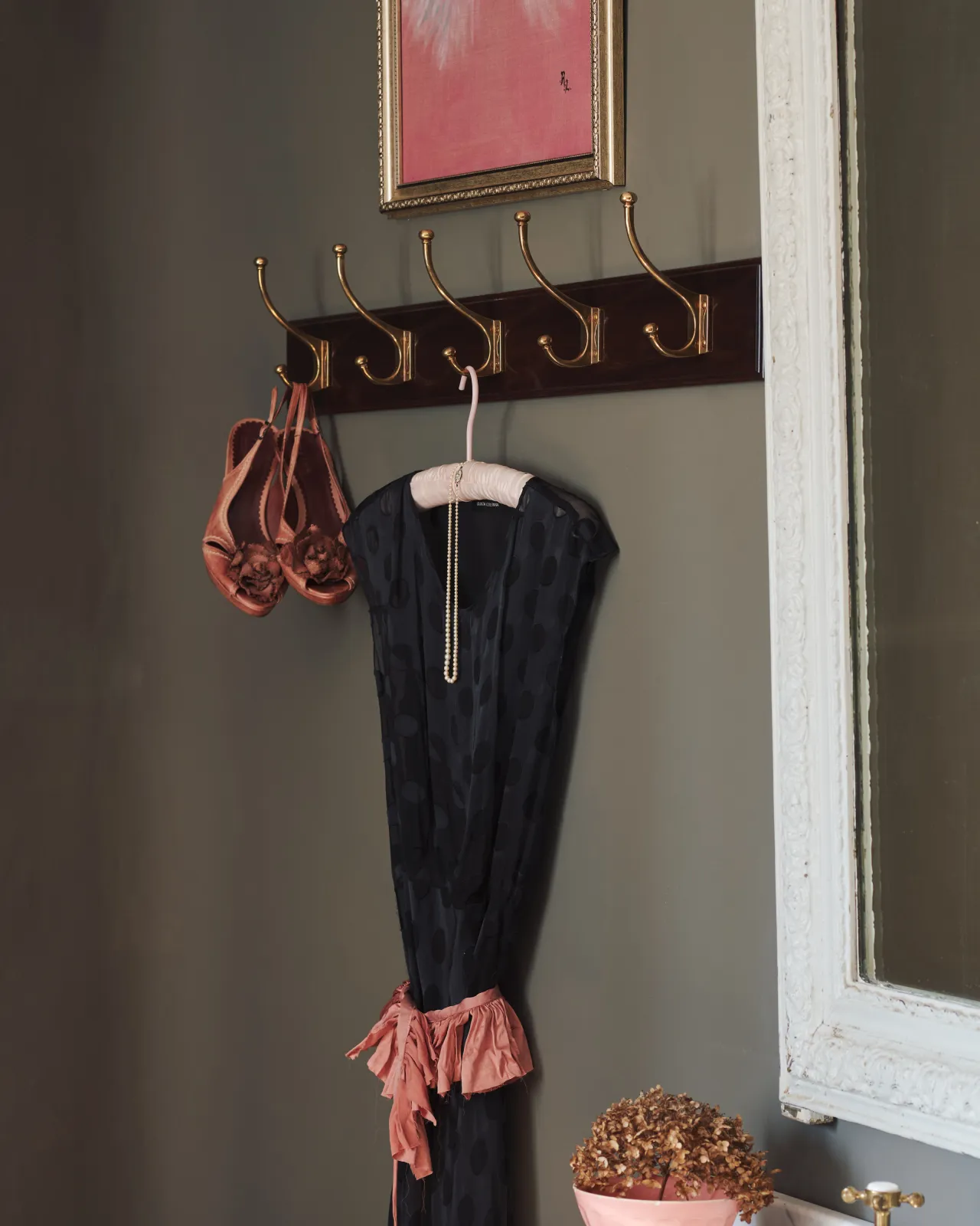An oblique view of a black lace dress and dusky pink shoes hanging from a Mahogany Finish Hook Rack with Edwardian brass hooks.