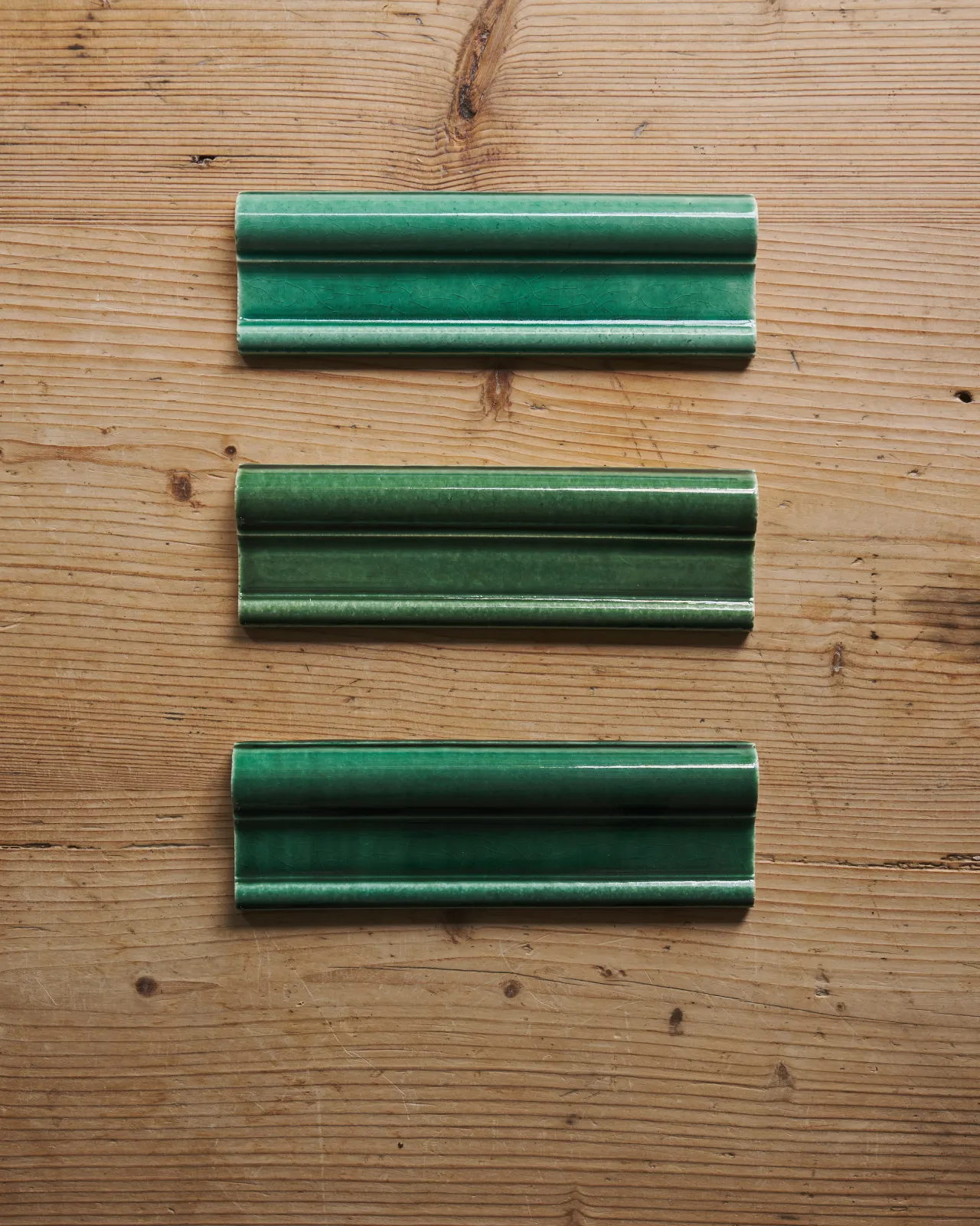 a top down view of a three emerald green border tiles on a wooden backdrop.