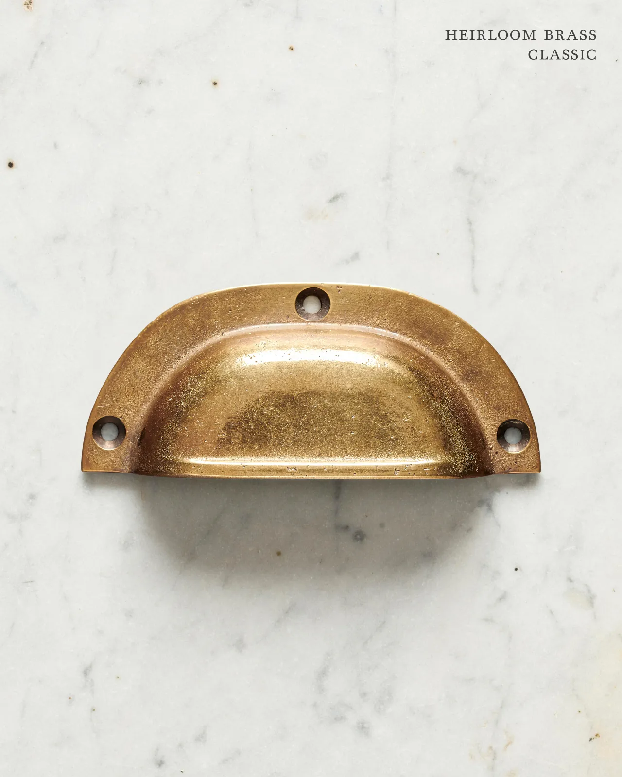 A classic cup handle for a kitchen cupboard or drawer with a warm burnished brass finish.