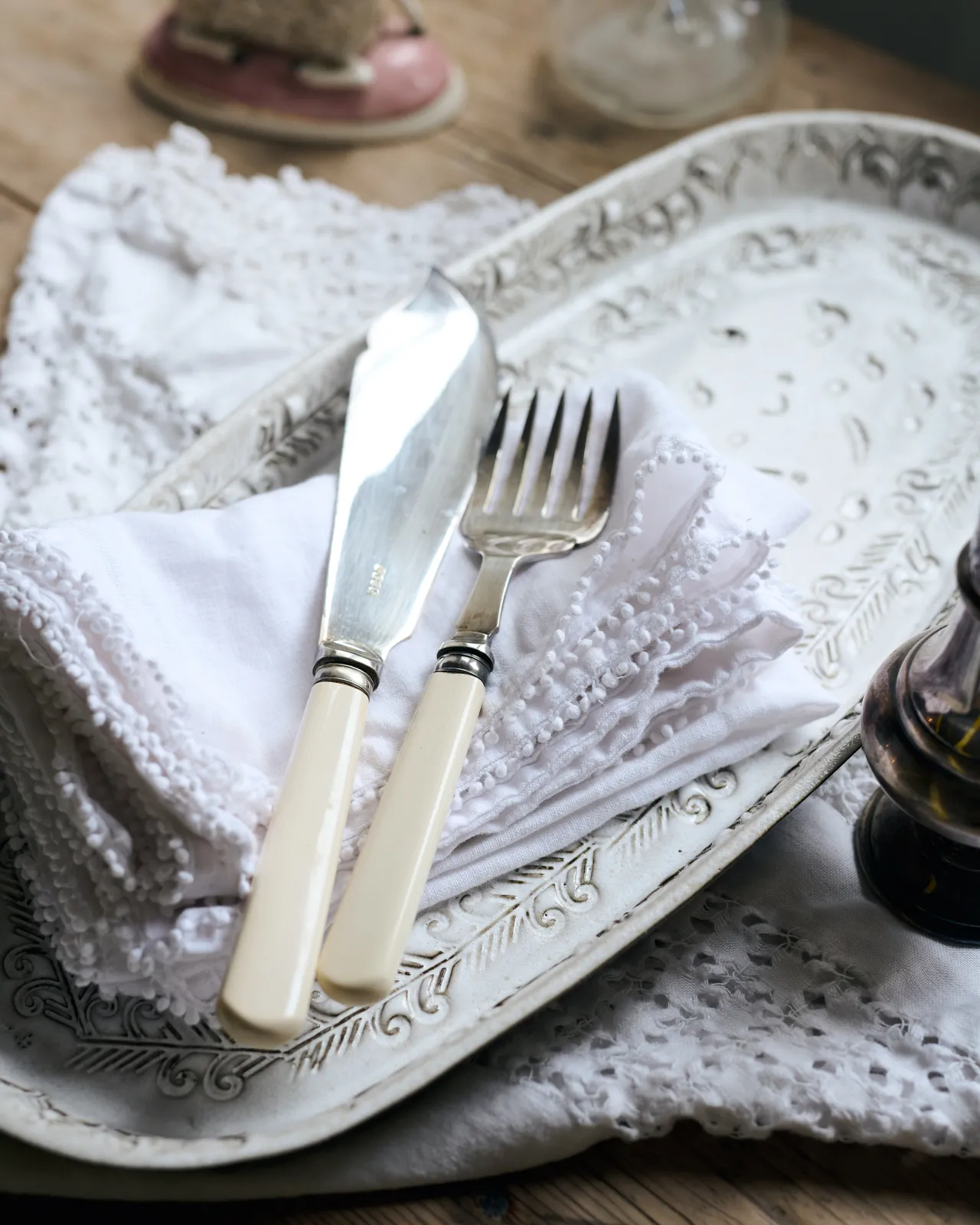 Vintage silverware, white linens on an oval-shaped handmade bohemian-style white ceramic platter with delicate impressions and surface patterns.