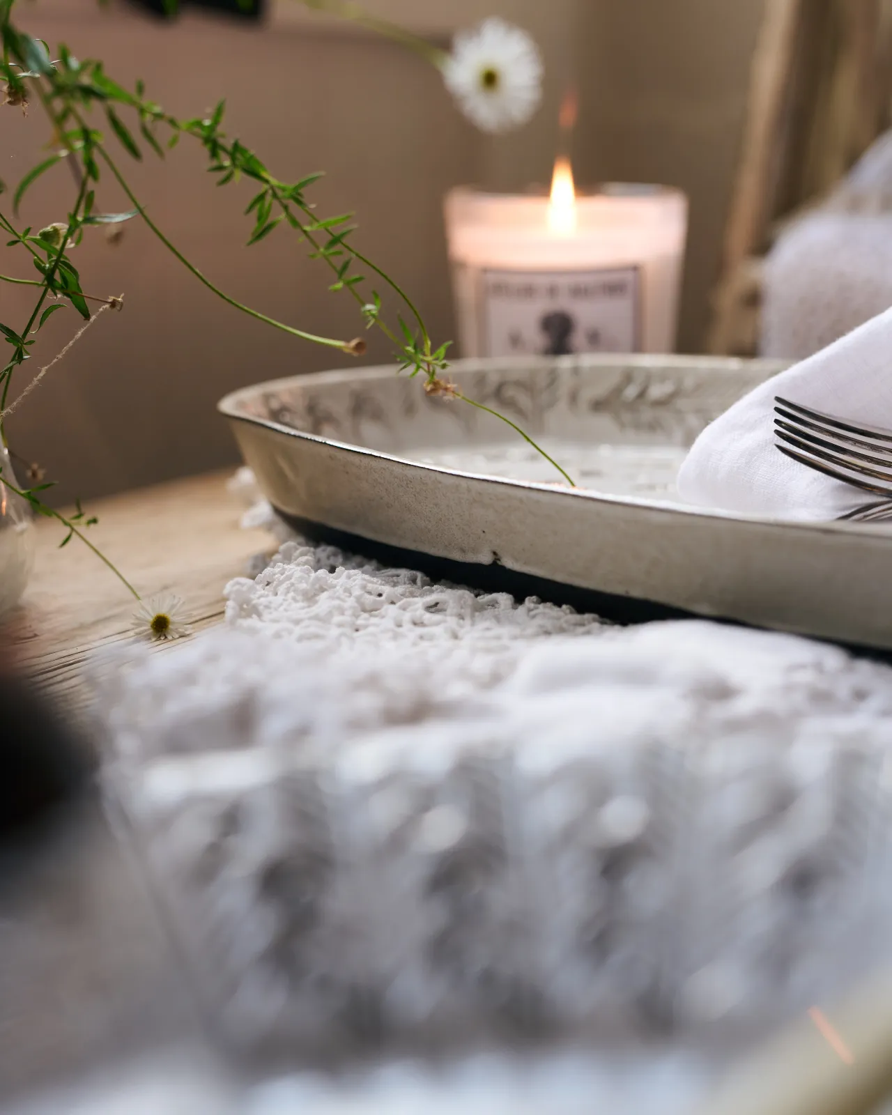 A profile view of oval-shaped handmade bohemian-style white ceramic platter, with a lit scented candle in the background.