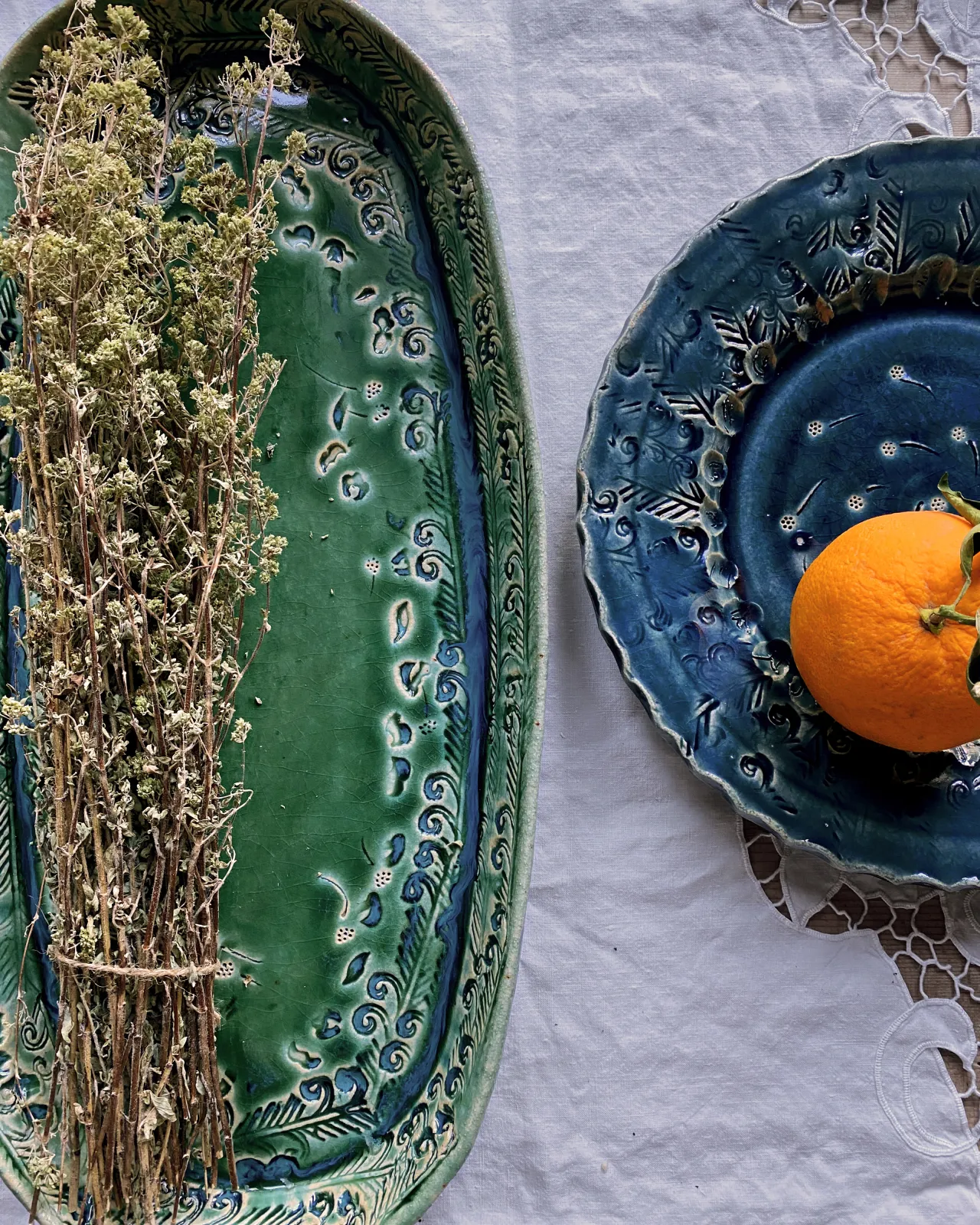 An overhead view of a green oval-shaped ceramic platter and a blue round-shaped ceramic platter with a single orange on top.