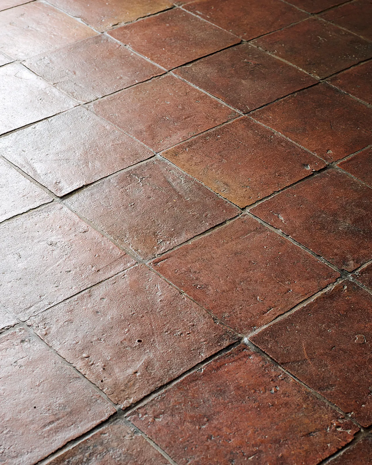 An oblique view of square terracotta flooring with an authentic aged finish.