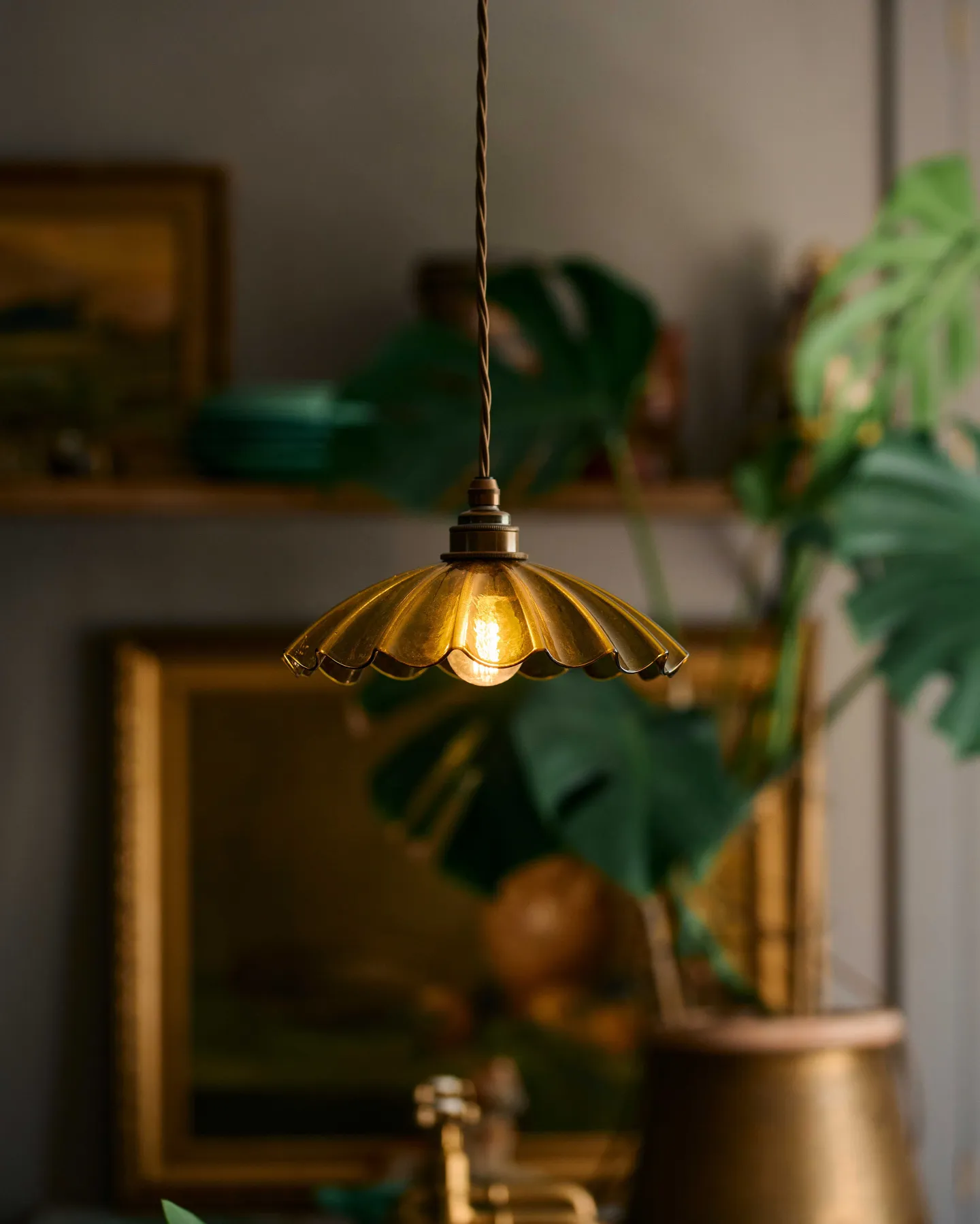 A chartreuse-coloured frilly glass pendant light hanging in an atmospheric kitchen with a large monstera plant.