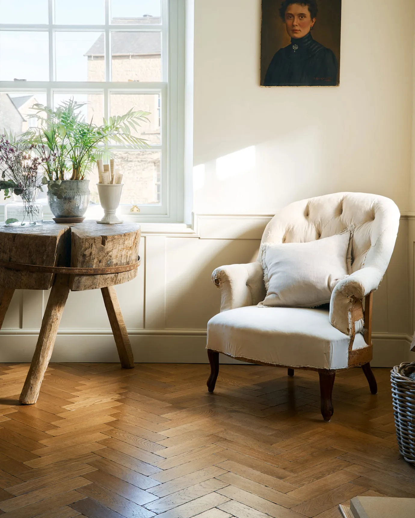 A quiet corner of a modern living room with a vintage wooden side table, a cream armchair, pillow, and the warm wooden Chatsworth Parquet floor.