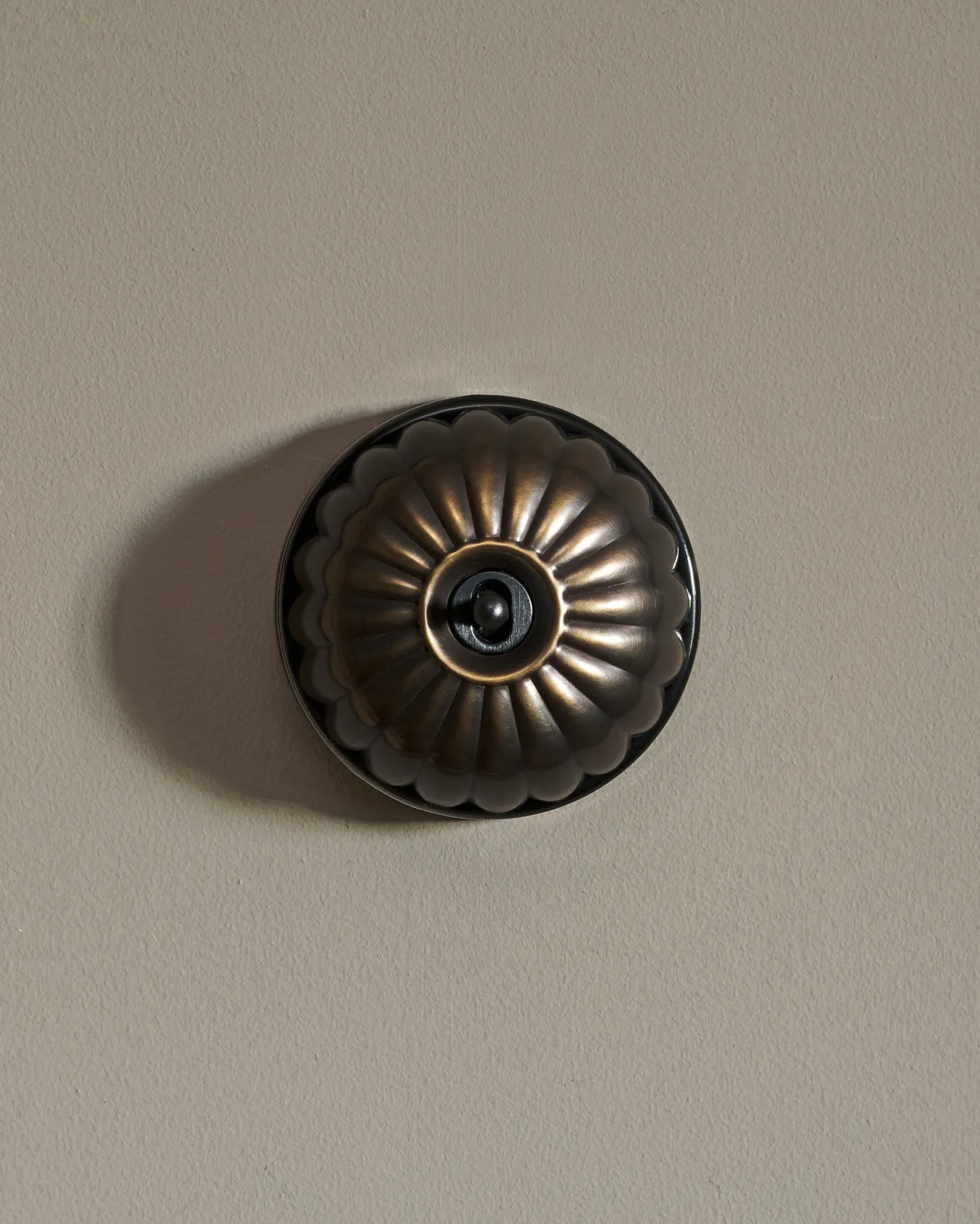 A straight-on view of a small 1 gang round-shaped toggle switch in a dark burnished brass finish with a black base.