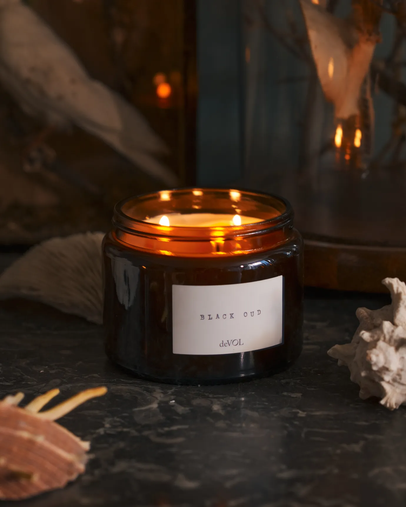 our candle on a grey table with sea shells around it.