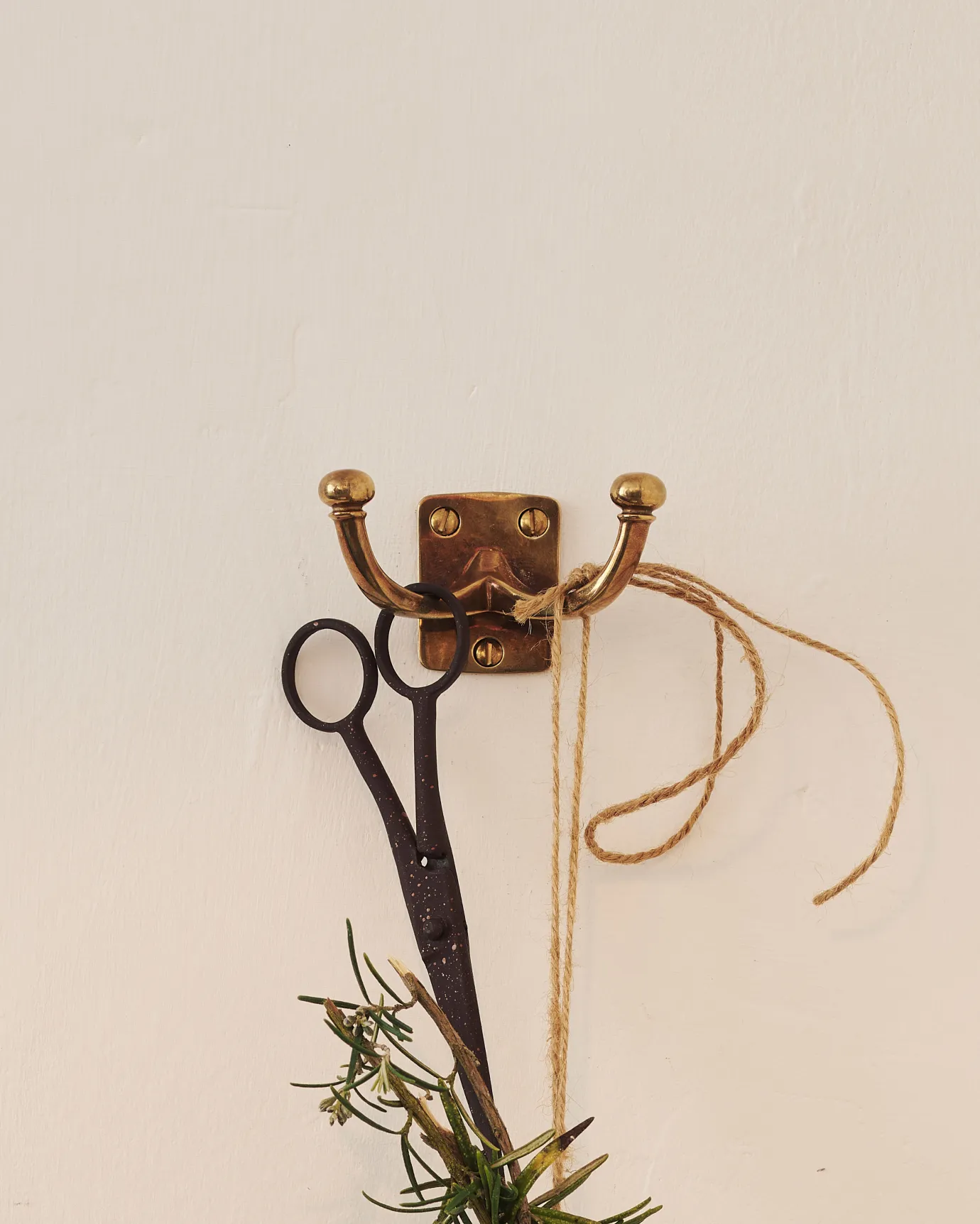 An Edwardian-style twin brass hook, fitted to a white painted wall.