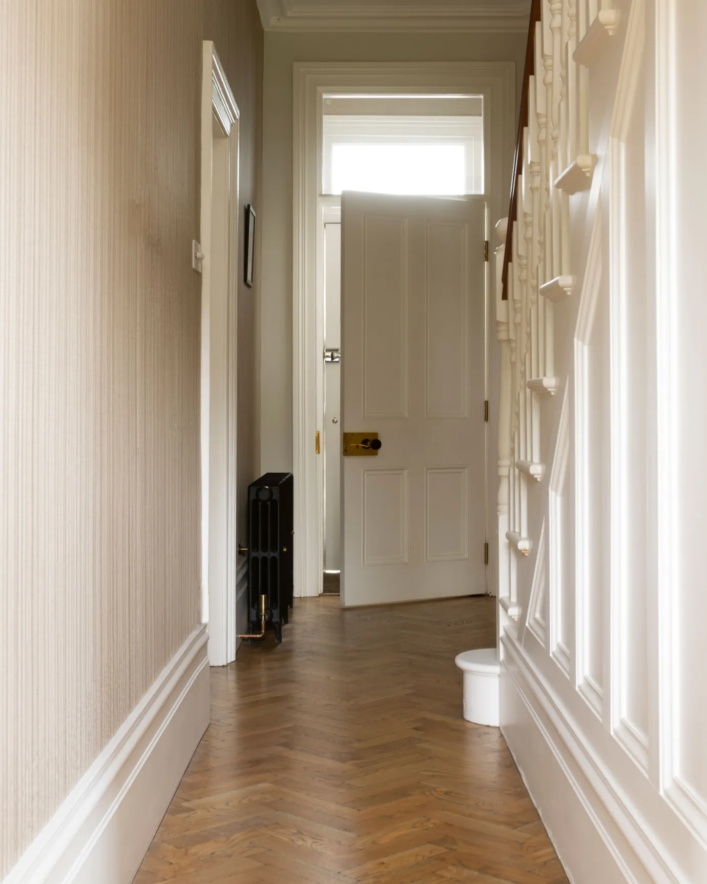 Looking down a hallway with traditional styling, striped wallpaper, white painted woodwork and oak parquet flooring with a warm aged finish.