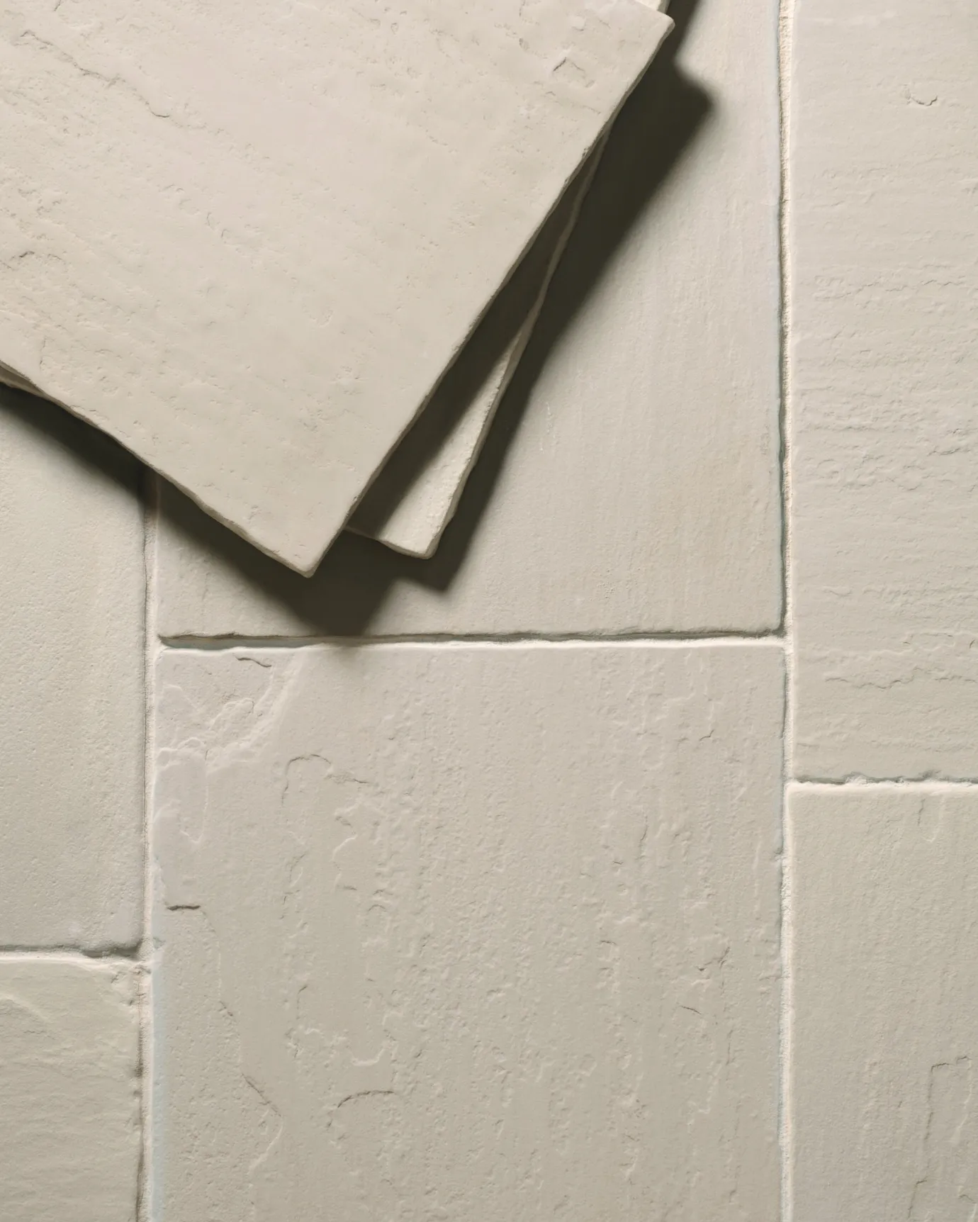 A close-up overhead view of a cream coloured sandstone floor, with two loose tiles stacked in one corner.